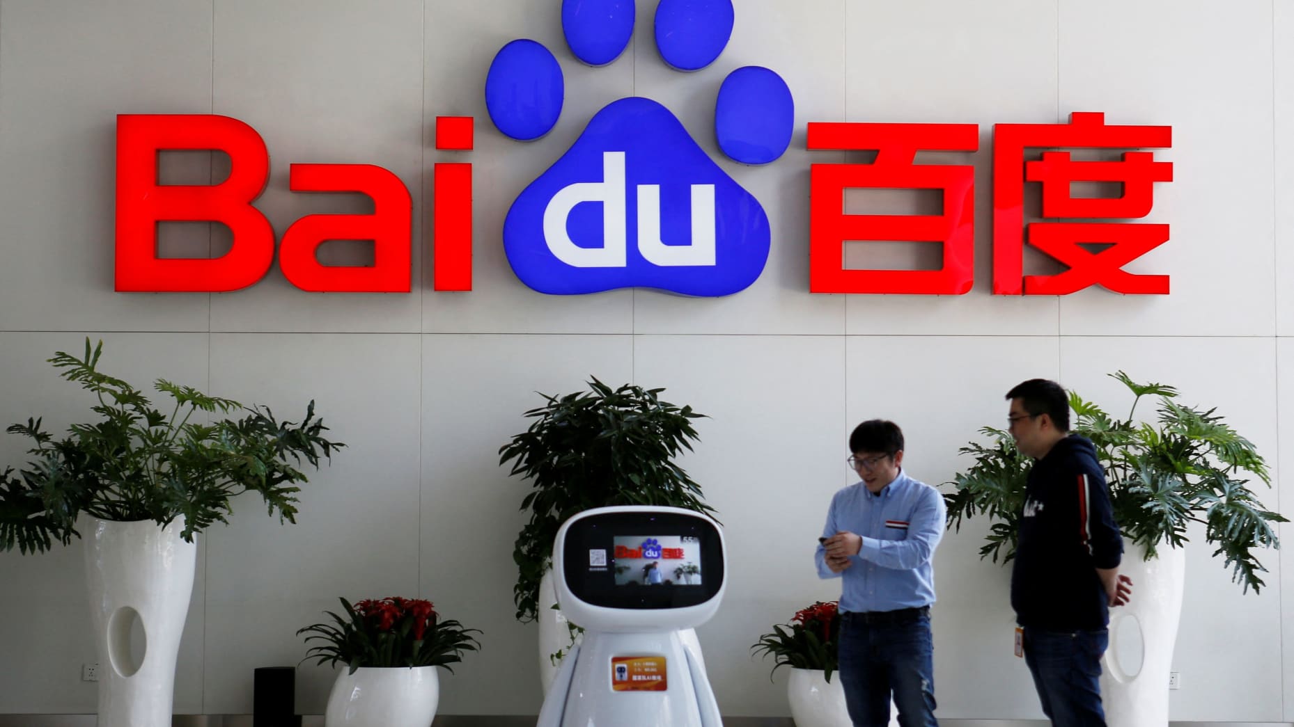Men interact with a Baidu AI robot near the company logo at its headquarters in Beijing, China April 23, 2021.
